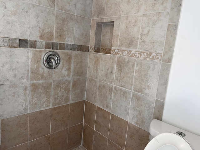 full bathroom featuring tiled shower and toilet