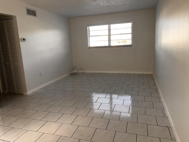 unfurnished room with baseboards, visible vents, and a textured ceiling