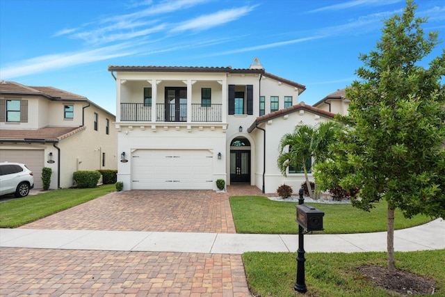 mediterranean / spanish-style home featuring decorative driveway, french doors, stucco siding, a front yard, and a balcony