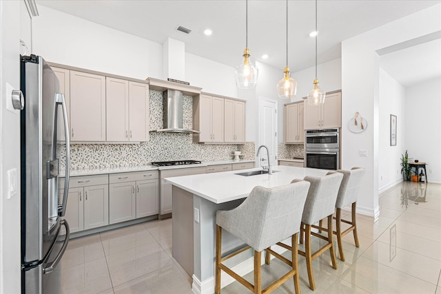 kitchen with light tile patterned floors, a sink, appliances with stainless steel finishes, backsplash, and wall chimney exhaust hood