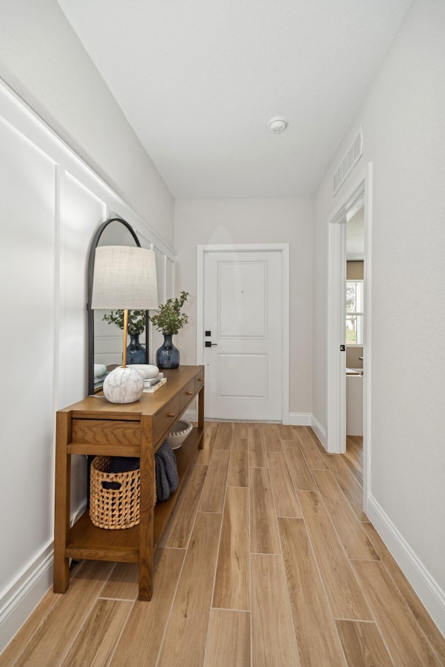 hall featuring visible vents, baseboards, and light wood-style floors