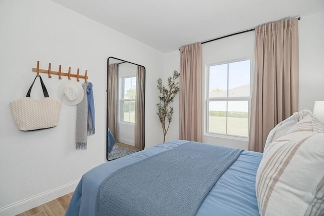 bedroom with multiple windows, wood finished floors, and baseboards