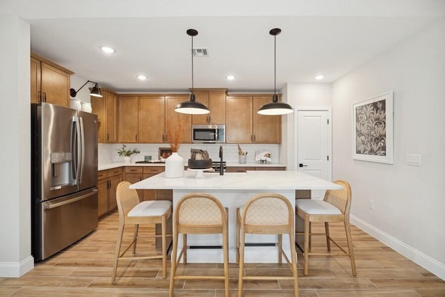 kitchen with visible vents, wood finish floors, a kitchen bar, brown cabinetry, and stainless steel appliances