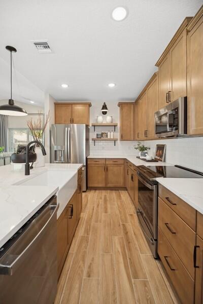 kitchen featuring visible vents, wood tiled floor, open shelves, a sink, and appliances with stainless steel finishes