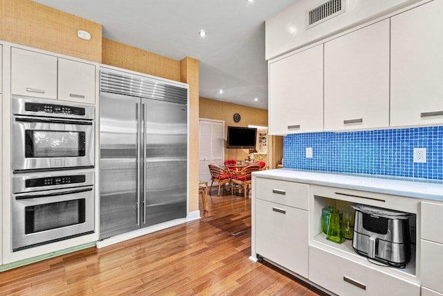 kitchen with tasteful backsplash, light wood-type flooring, light countertops, appliances with stainless steel finishes, and white cabinetry