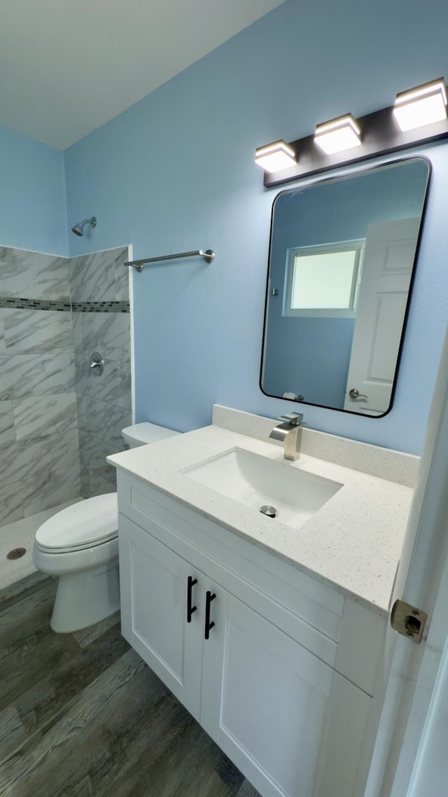 bathroom with toilet, a tile shower, wood finished floors, and vanity