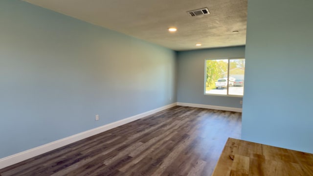 empty room with dark wood-style floors, baseboards, visible vents, and a textured ceiling