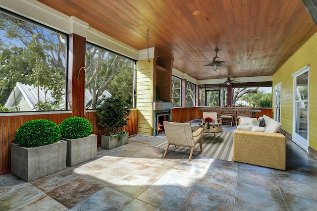 sunroom with ceiling fan, wood ceiling, and a lit fireplace