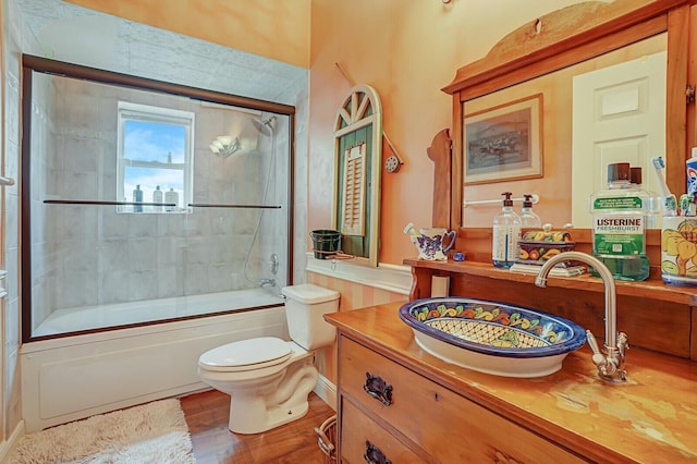 full bath with bath / shower combo with glass door, toilet, vanity, and wood finished floors