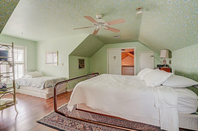 bedroom with visible vents, wallpapered walls, vaulted ceiling, wood finished floors, and a textured ceiling