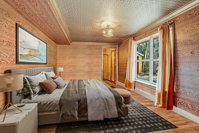 bedroom featuring wallpapered walls, crown molding, baseboards, wood finished floors, and an ornate ceiling