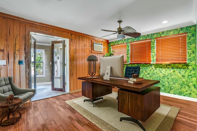 office area featuring a wall unit AC, a ceiling fan, wood finished floors, baseboards, and ornamental molding