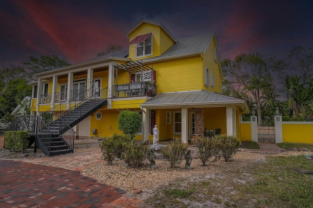 view of front facade with a gate, fence, covered porch, metal roof, and stairs