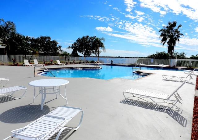 pool with a patio, a water view, and fence