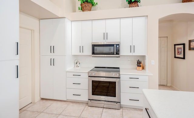 kitchen featuring light tile patterned floors, arched walkways, stainless steel appliances, light countertops, and white cabinetry