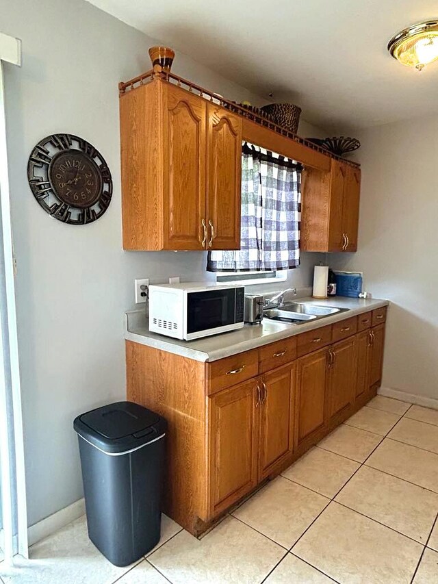 kitchen with brown cabinetry, light tile patterned floors, light countertops, and white microwave