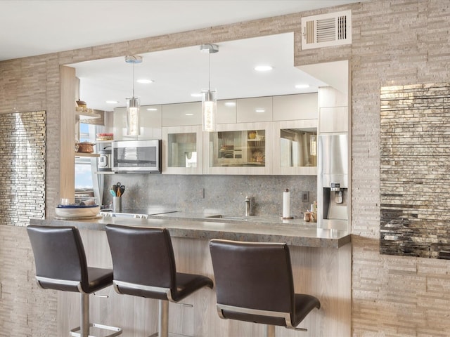 bar featuring tasteful backsplash, stainless steel microwave, visible vents, and decorative light fixtures