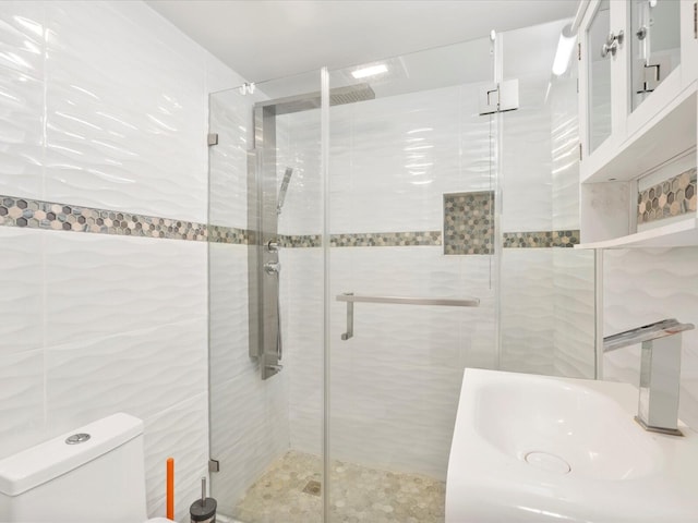 bathroom with tile walls, a sink, a shower stall, and toilet