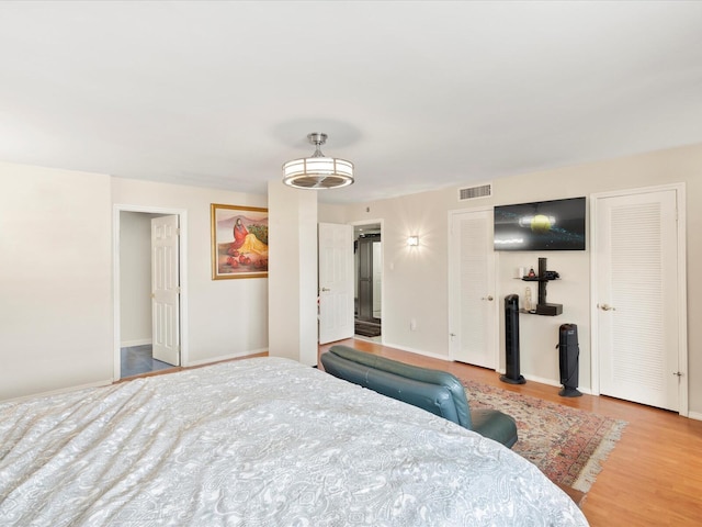 bedroom with two closets, baseboards, visible vents, and wood finished floors