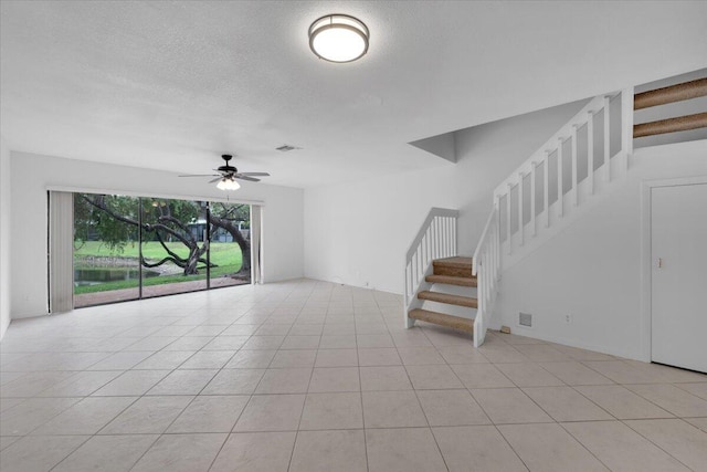 unfurnished living room featuring light tile patterned floors, a textured ceiling, ceiling fan, and stairs