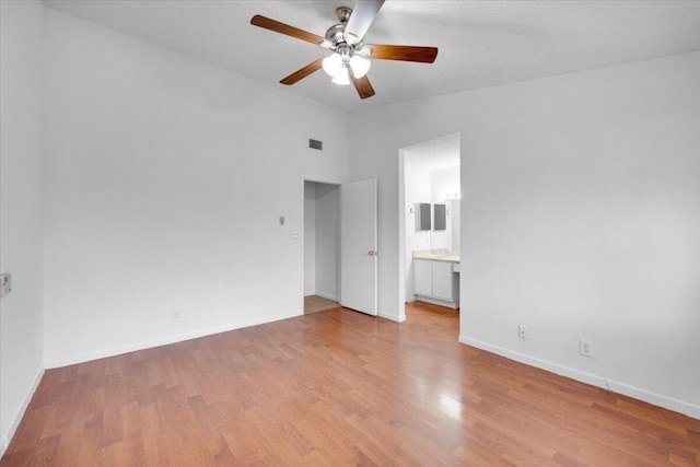 spare room featuring light wood finished floors, visible vents, baseboards, and vaulted ceiling