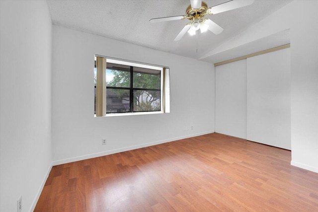 spare room with lofted ceiling, a ceiling fan, a textured ceiling, wood finished floors, and baseboards