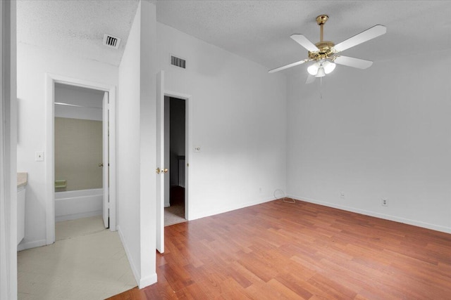 empty room with visible vents, light wood-style flooring, a ceiling fan, a textured ceiling, and baseboards