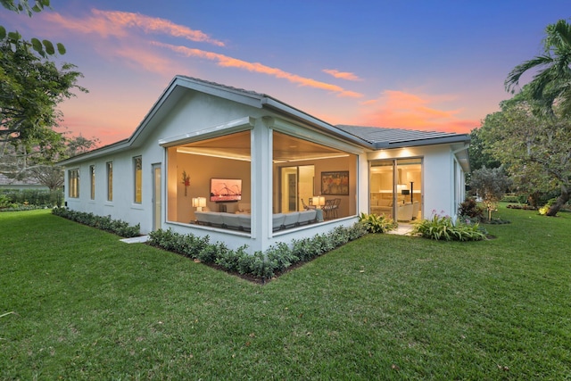 back of property at dusk with a lawn and stucco siding