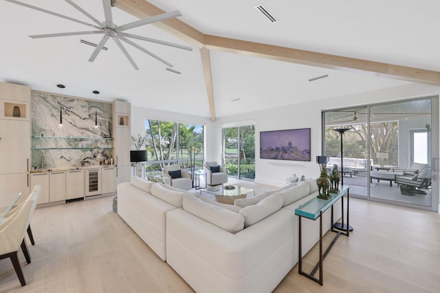 living room featuring lofted ceiling with beams, light wood finished floors, wine cooler, and a healthy amount of sunlight