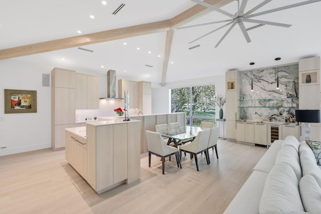 kitchen featuring light wood-style flooring, lofted ceiling with beams, backsplash, modern cabinets, and wall chimney exhaust hood