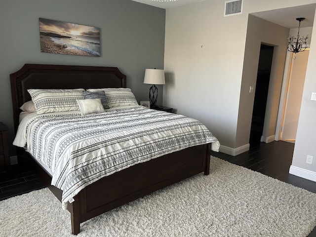 bedroom featuring a notable chandelier, wood finished floors, visible vents, and baseboards