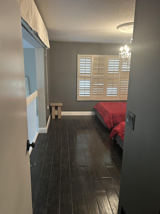 bedroom with a chandelier, dark wood finished floors, a textured ceiling, and baseboards