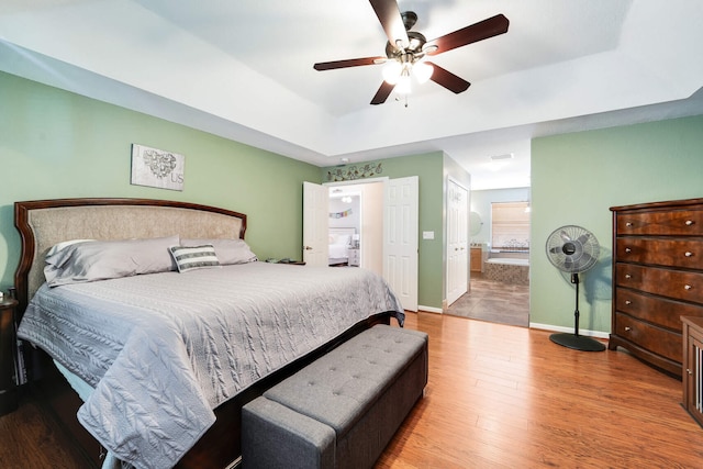 bedroom with baseboards, connected bathroom, a tray ceiling, ceiling fan, and wood finished floors