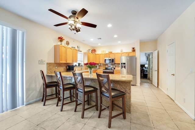 kitchen with backsplash, light brown cabinets, light countertops, appliances with stainless steel finishes, and a peninsula