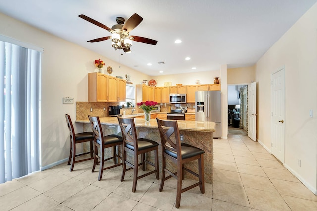 kitchen featuring a peninsula, a ceiling fan, appliances with stainless steel finishes, light brown cabinets, and backsplash