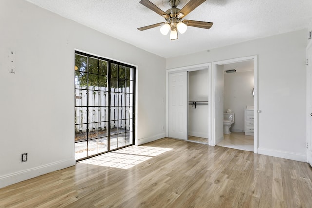 unfurnished bedroom with a textured ceiling, ensuite bath, wood finished floors, and baseboards