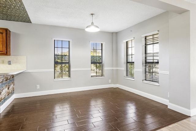 unfurnished dining area with a textured ceiling, baseboards, and wood finished floors