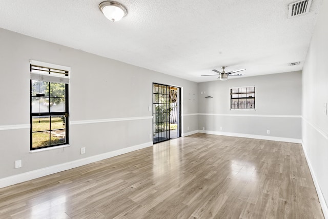 spare room with a textured ceiling, wood finished floors, visible vents, and a healthy amount of sunlight