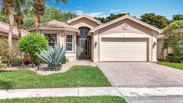 view of front of home with decorative driveway, stucco siding, a front yard, a garage, and a tiled roof