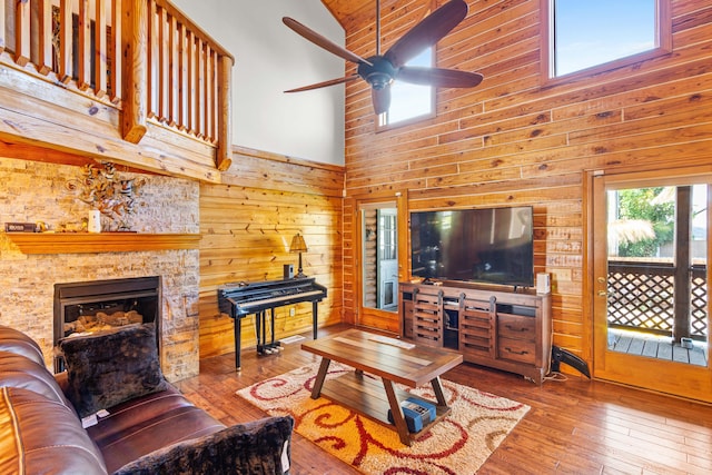 living area featuring wooden walls, a fireplace, a towering ceiling, a ceiling fan, and wood-type flooring