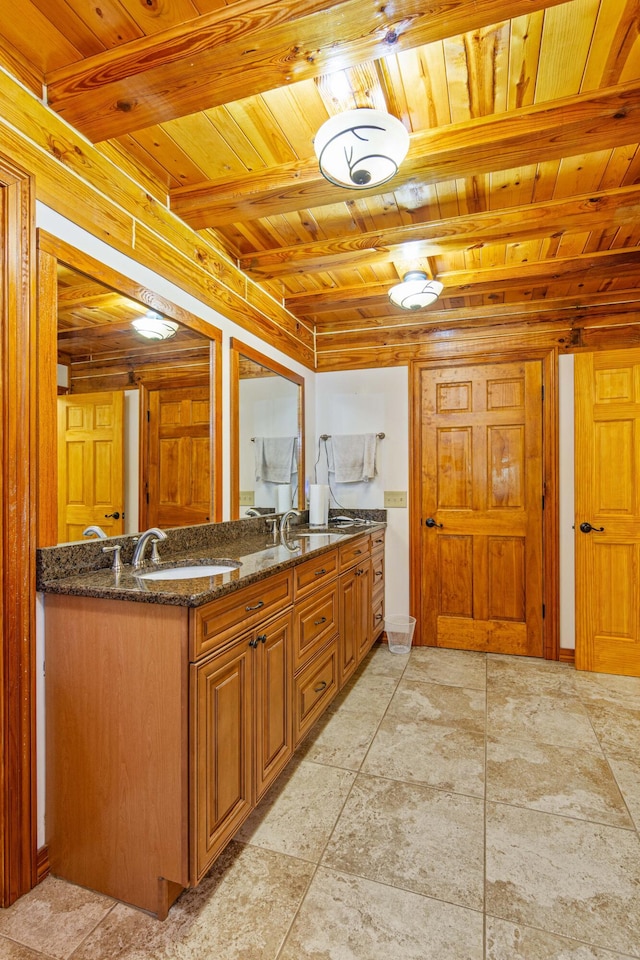 kitchen featuring brown cabinets, a sink, dark stone countertops, wooden ceiling, and beamed ceiling