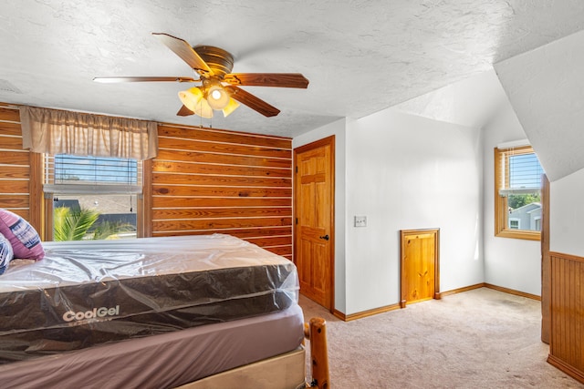 carpeted bedroom with a textured ceiling, ceiling fan, baseboards, and wooden walls