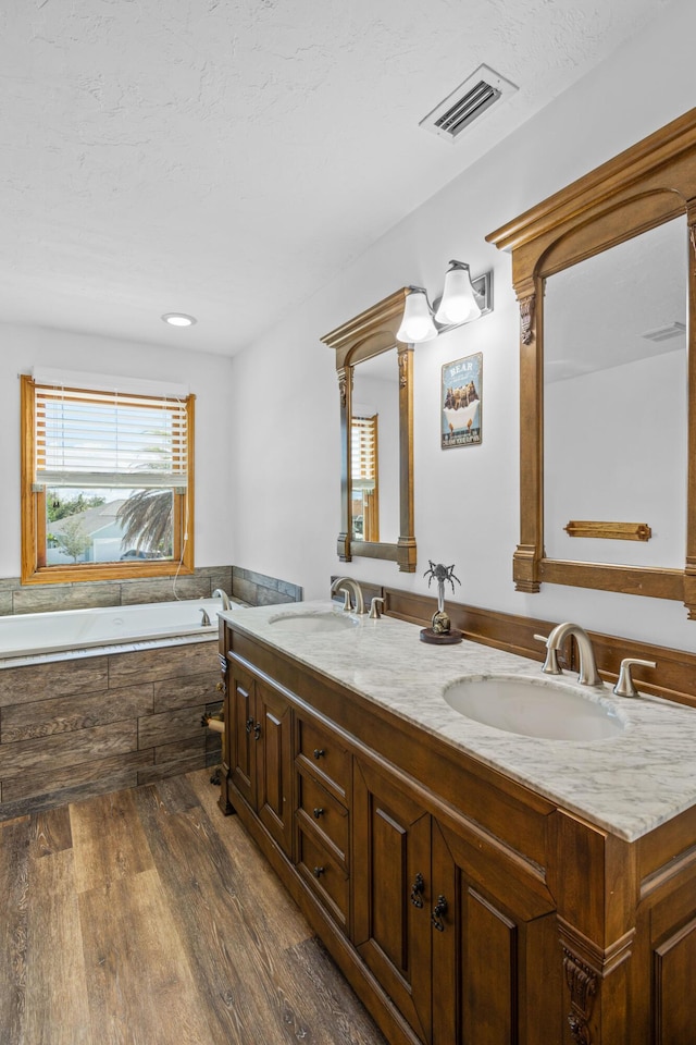 bathroom with visible vents, a sink, a garden tub, and wood finished floors