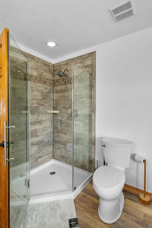 bathroom featuring toilet, wood finished floors, visible vents, baseboards, and a stall shower