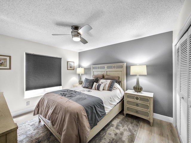 bedroom featuring baseboards, ceiling fan, wood finished floors, a closet, and a textured ceiling