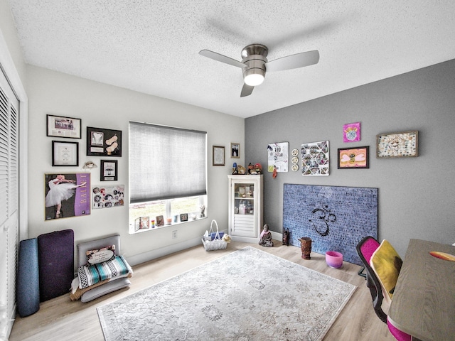 recreation room featuring ceiling fan, a textured ceiling, and wood finished floors