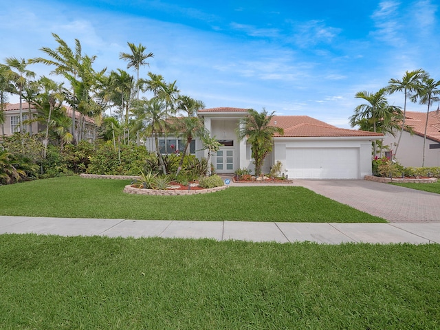 mediterranean / spanish house with a front lawn, a tile roof, stucco siding, decorative driveway, and an attached garage