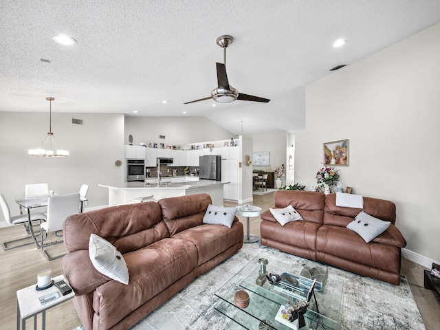 living room featuring light wood finished floors, visible vents, ceiling fan with notable chandelier, and vaulted ceiling