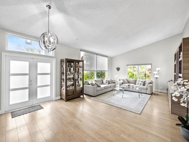 unfurnished living room featuring light wood-type flooring, a textured ceiling, french doors, lofted ceiling, and a chandelier