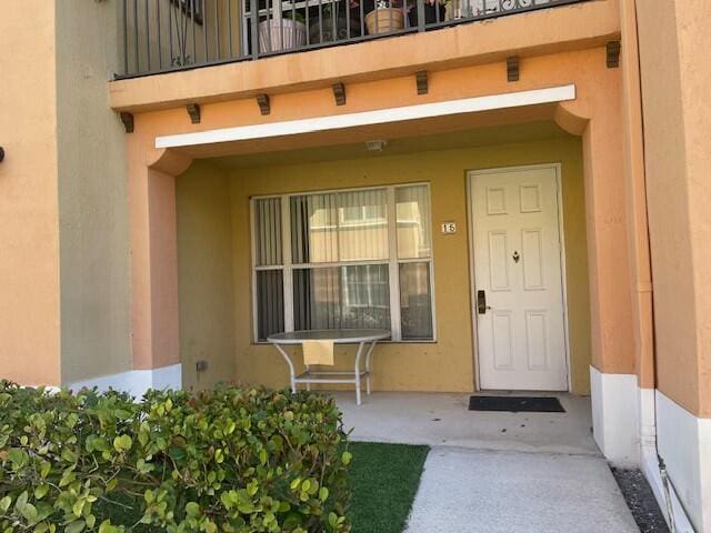 view of exterior entry with a balcony, covered porch, and stucco siding